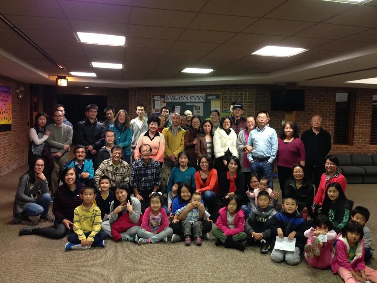 Group photo of about 50 adults and children in a church fellowship hall, taken during Dr. Clement Yeung’s visit