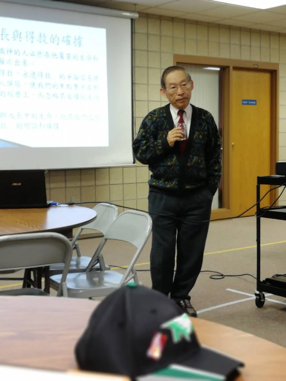 Pastor Tsu-Kung Chuang speaking beside a projected slide in Chinese