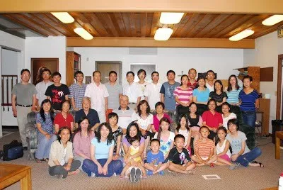 Group photo of about 45 adults and children gathered in a living room